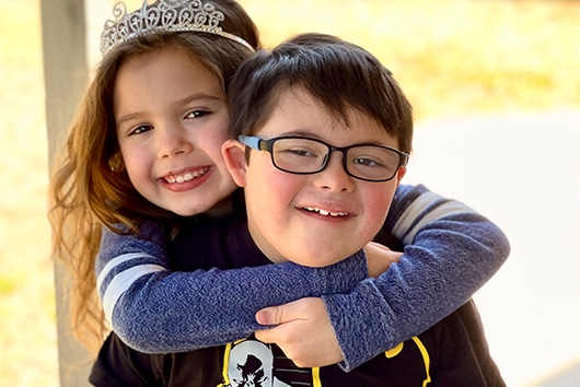 young boy with down syndrome and his sister giving him a hug around the neck.
