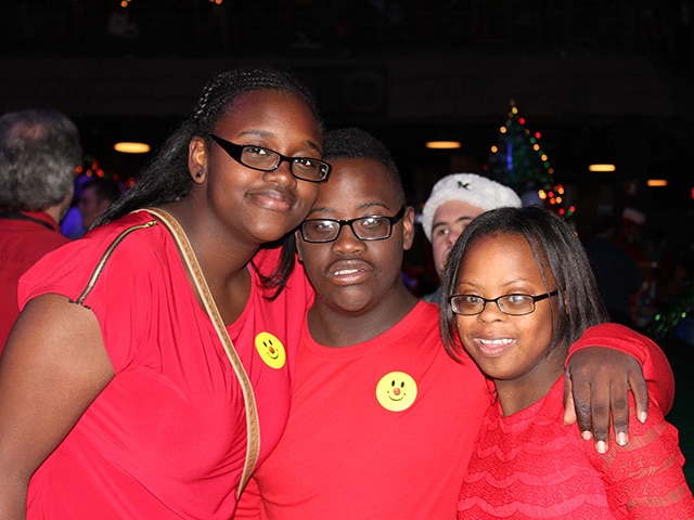 adult male with down syndrome and his two sisters with their arms around each other.