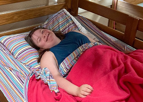 young girl with Down syndrome smiling and laying down on the bottom bunk